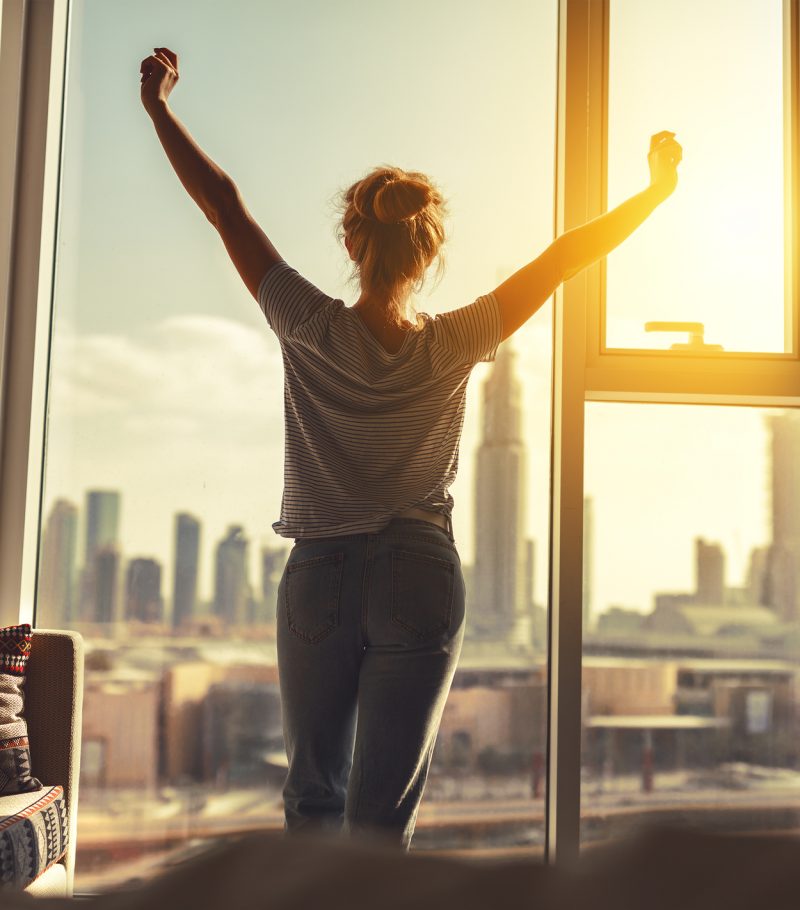 happy woman stretches and opens the curtains at window in morning